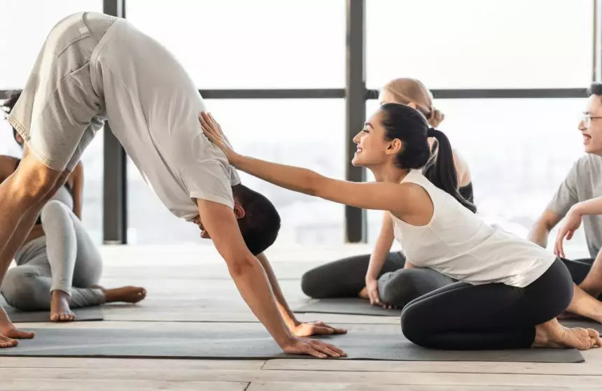 Female coach correcting yoga beginner at group class training in studio