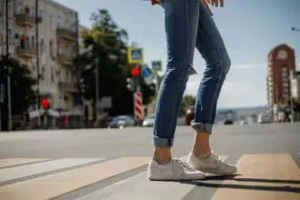 Young girl dressed in jeans and sneakers is crossing the road with a backpack in a city street on a
